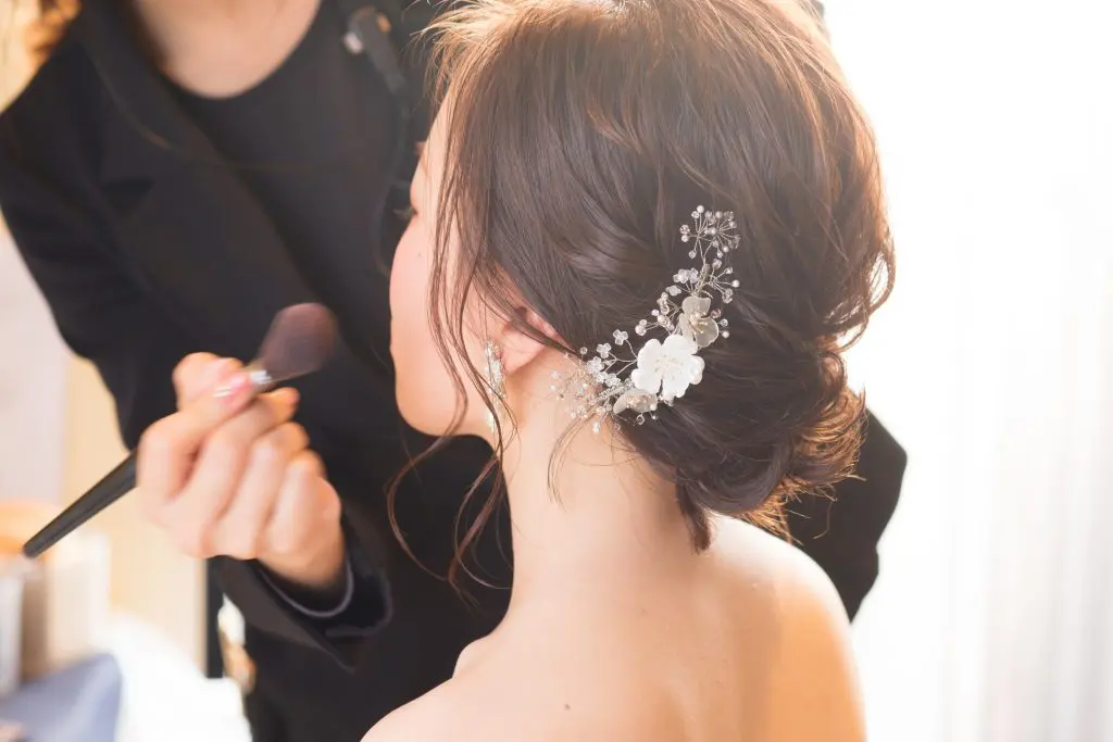 支度の最中、髪に花を挿した新婦がメイクを受けている後ろ姿