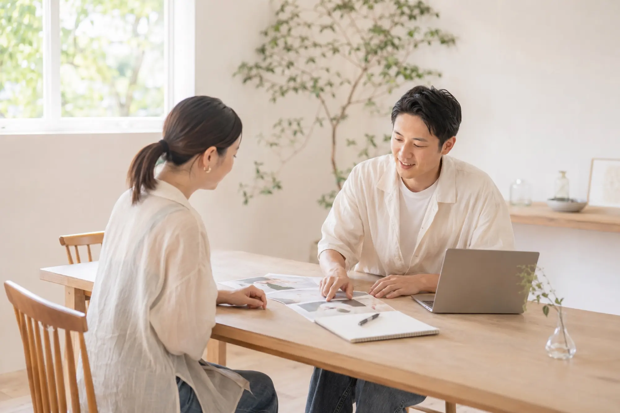 明るい部屋のテーブルで、資料を広げて打ち合わせをしている二人
