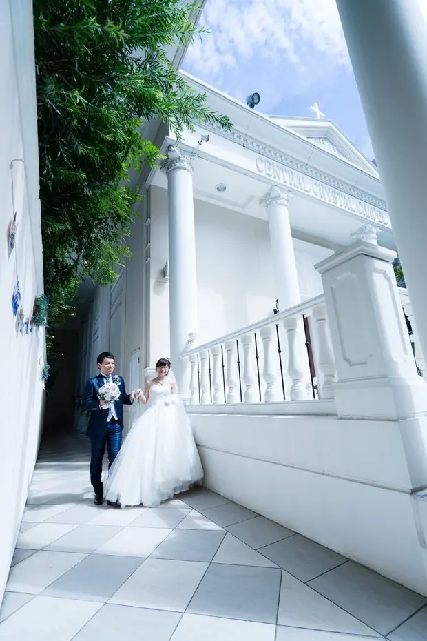 夏の光の中、白い教会の前を歩く新郎新婦