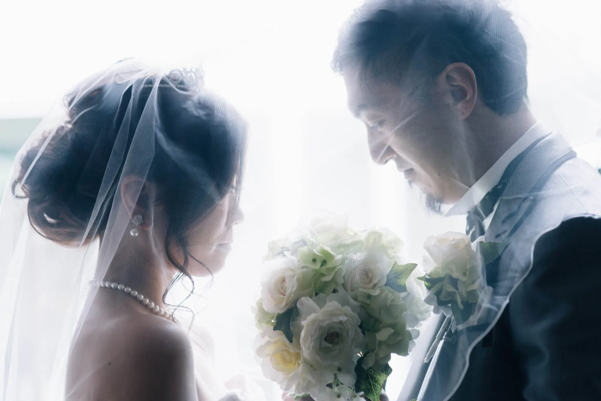光の中で、ブーケを挟んで静かに向き合う新郎新婦